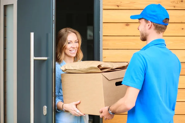 Uomo di consegna sorridente in uniforme blu che consegna pacchi al destinatario - concetto di servizio di corriere — Foto Stock