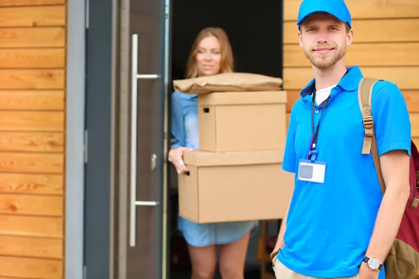 Lächelnder Zusteller in blauer Uniform bringt Paketkasten zum Empfänger - Kurierdienst-Konzept — Stockfoto