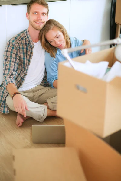 Unga par som flyttar i nya hem. Sitter på golvet och avkopplande efter uppackning. Ser något på laptop — Stockfoto