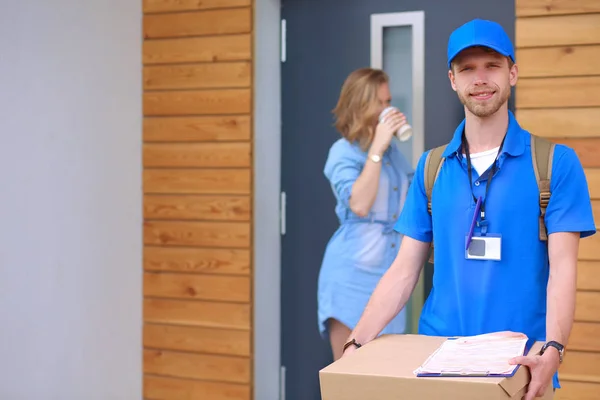 Leende leverans man i blå uniform leverera paket låda till mottagaren - kurir service koncept — Stockfoto