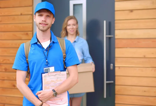 Repartidor sonriente en uniforme azul que entrega la caja de paquetes al destinatario - concepto de servicio de mensajería — Foto de Stock