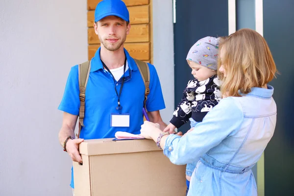 Lächelnder Zusteller in blauer Uniform bringt Paketkasten zum Empfänger - Kurierdienst-Konzept — Stockfoto