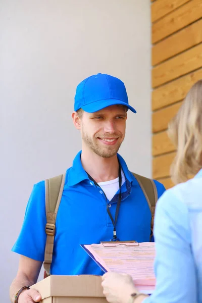 Repartidor sonriente en uniforme azul que entrega la caja de paquetes al destinatario - concepto de servicio de mensajería —  Fotos de Stock