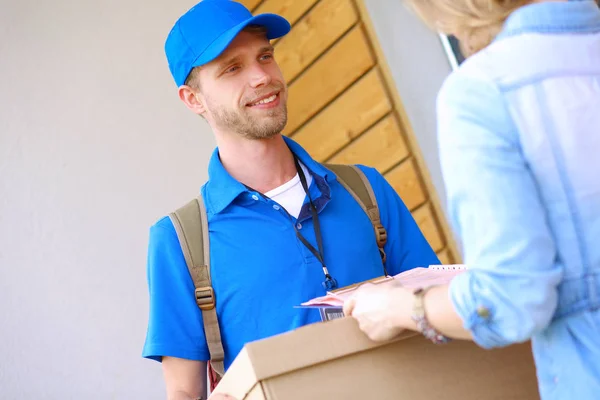 Uomo di consegna sorridente in uniforme blu che consegna pacchi al destinatario - concetto di servizio di corriere — Foto Stock