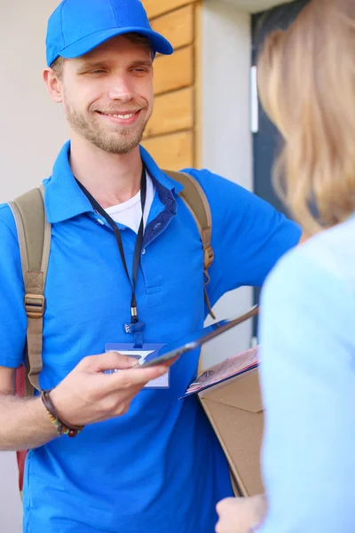 Repartidor sonriente en uniforme azul que entrega la caja de paquetes al destinatario - concepto de servicio de mensajería — Foto de Stock