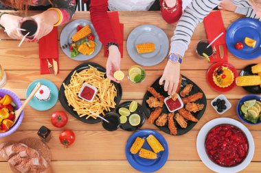 Ahşap masada otururken birlikte yemek yiyen bir grup insanın üst düzey görüntüsü. Masada yemek var. İnsanlar fast food yiyor..