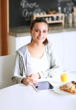 Mutfakta portakal suyu ve tableti olan genç bir kadın..