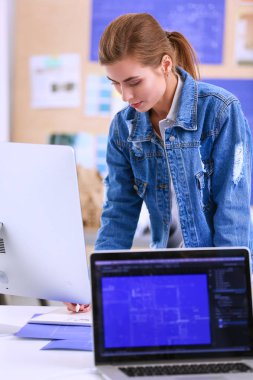 Enstrümanlar, planlar ve dizüstü bilgisayarlarla masanın yanında duran genç bir kadın..