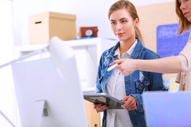 Masanın yanında duran iki genç kadın enstrüman, plan ve dizüstü bilgisayarla.