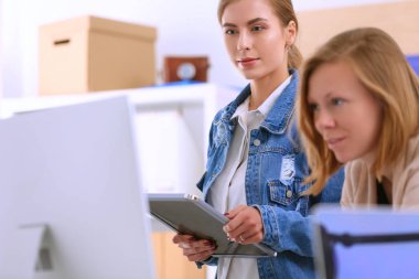 Masanın yanında duran iki genç kadın enstrüman, plan ve dizüstü bilgisayarla.