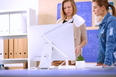 Masanın yanında duran iki genç kadın enstrüman, plan ve dizüstü bilgisayarla.