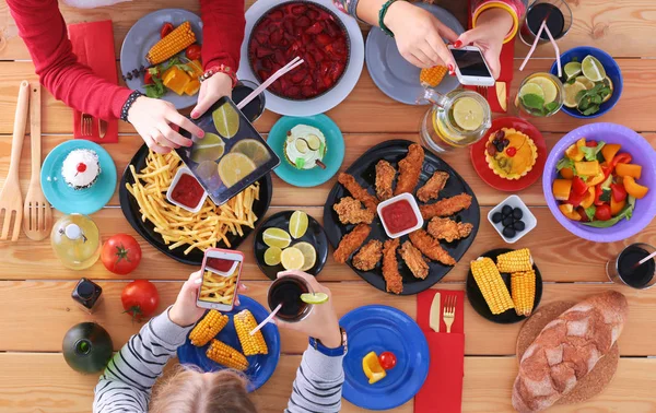 Ahşap masada otururken birlikte yemek yiyen bir grup insanın üst düzey görüntüsü. Masada yemek var. İnsanlar fast food yiyor..