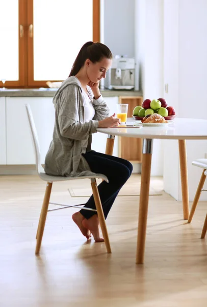 Mujer joven con jugo de naranja y tableta en la cocina. — Foto de Stock