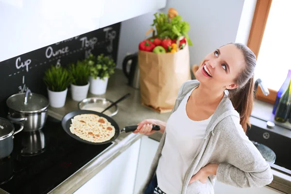 Mujer joven prepara panqueques en la cocina mientras está de pie cerca de la mesa. Mujer en la cocina. Cocinar en la cocina. —  Fotos de Stock