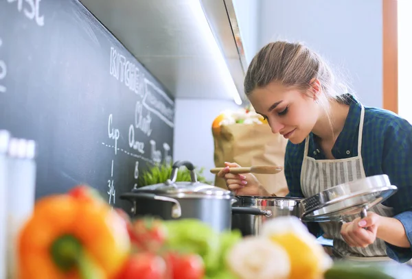 Mujer joven parada junto a la estufa en la cocina . — Foto de Stock