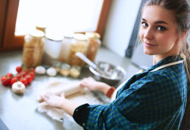 Güzel bir kadın mutfakta pasta pişiriyor. Masanın yanında duruyor..
