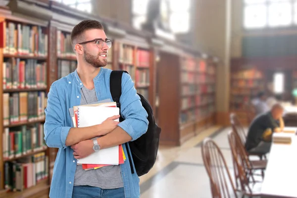 En manlig student med en skolväska anläggning böcker i biblioteket — Stockfoto