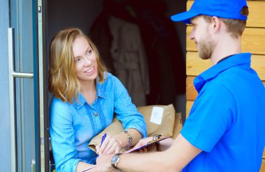 Mavi üniformalı gülümseyen kurye servis konseptine paket kutusu teslim eden teslimatçı.
