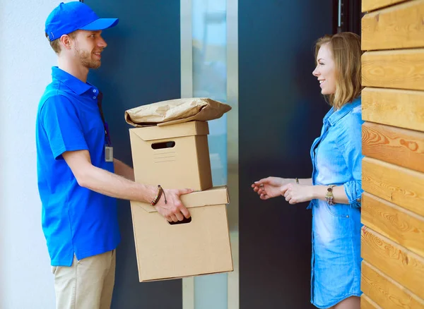Mavi üniformalı gülümseyen kurye servis konseptine paket kutusu teslim eden teslimatçı.