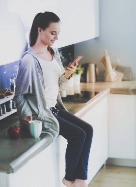 modern mutfakta otururken cep telefonu kullanan kadın.