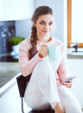 modern mutfakta otururken cep telefonu kullanan kadın.