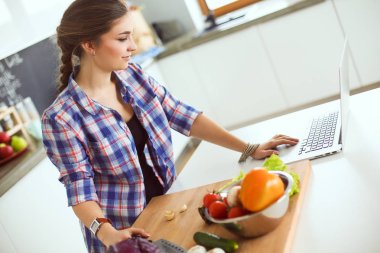 Masanın yanındaki mutfakta sebze doğrayan genç bir kadın..