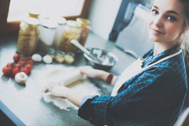 Güzel bir kadın mutfakta pasta pişiriyor. Masanın yanında duruyor..
