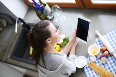 Güzel bir kadın mutfakta pasta pişiriyor. Masanın yanında duruyor..