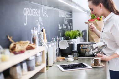 Mutfakta sobanın yanında duran genç bir kadın. Mutfakta yemek pişiren kadın..