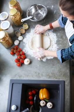 Güzel bir kadın mutfakta pasta pişiriyor. Masanın yanında duruyor..