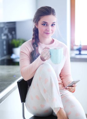 modern mutfakta otururken cep telefonu kullanan kadın.