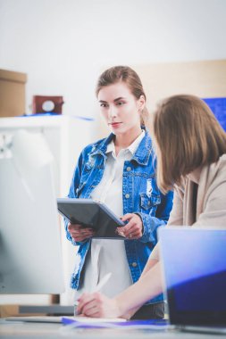 Masanın yanında duran iki genç kadın enstrüman, plan ve dizüstü bilgisayarla.