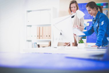 Masanın yanında duran iki genç kadın enstrüman, plan ve dizüstü bilgisayarla.