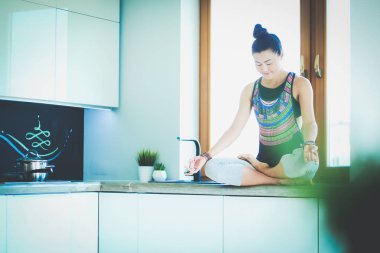 Lotus pozisyonunda mutfak masasında oturan genç güzel kadın. Kadın. Yoga