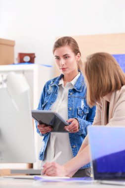 Masanın yanında duran iki genç kadın enstrüman, plan ve dizüstü bilgisayarla.