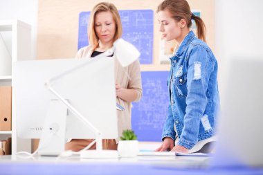 Masanın yanında duran iki genç kadın enstrüman, plan ve dizüstü bilgisayarla.