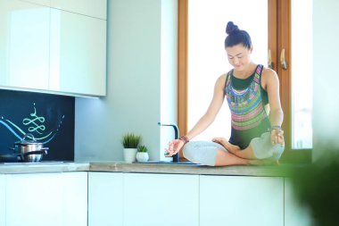 Lotus pozisyonunda mutfak masasında oturan genç güzel kadın. Kadın. Yoga