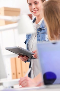 Masanın yanında duran iki genç kadın enstrüman, plan ve dizüstü bilgisayarla.