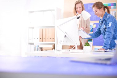 Masanın yanında duran iki genç kadın enstrüman, plan ve dizüstü bilgisayarla.