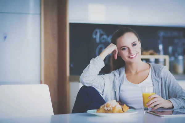 Mujer joven con jugo de naranja y tableta en la cocina. —  Fotos de Stock