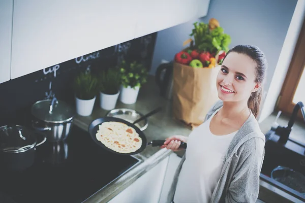 Young woman prepares pancakes in the kitchen while standing near the table. Woman in the kitchen. Cooking at kitchen. — Stock Photo, Image