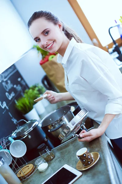 Mujer joven parada junto a la estufa en la cocina. Mujer cocinando en la cocina . —  Fotos de Stock