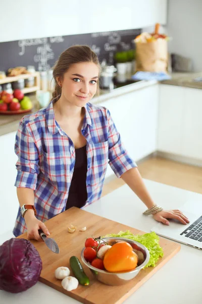 Masanın yanındaki mutfakta sebze doğrayan genç bir kadın..