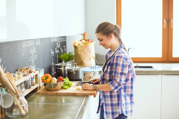 Ung kvinna skära grönsaker i köket nära skrivbordet. — Stockfoto