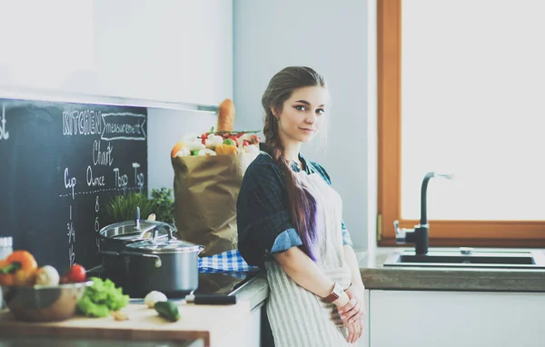 Ung kvinna står vid spisen i köket . — Stockfoto