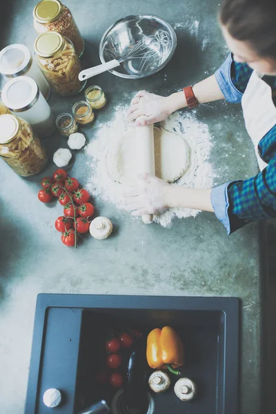 Güzel bir kadın mutfakta pasta pişiriyor. Masanın yanında duruyor..
