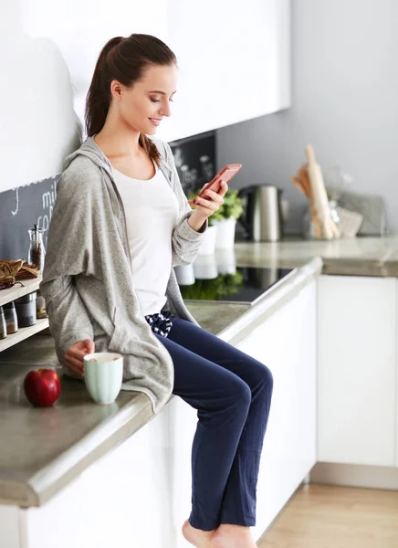 Женщина с помощью мобильного телефона сидит на современной кухне . — стоковое фото