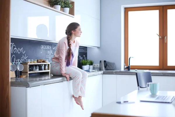 Jovem mulher sentada na mesa na cozinha . — Fotografia de Stock