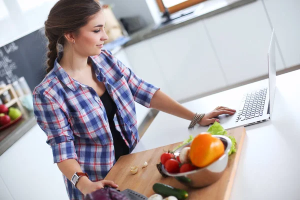Masanın yanındaki mutfakta sebze doğrayan genç bir kadın..