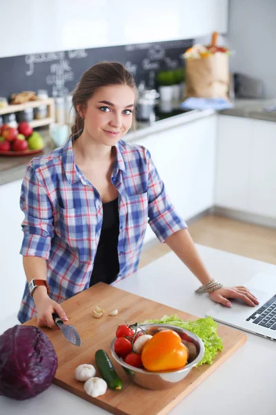 Jovem mulher cortando legumes na cozinha perto da mesa. — Fotografia de Stock